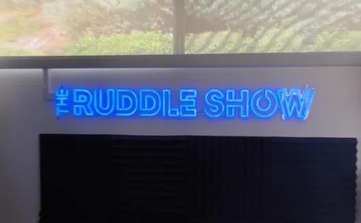 The Ruddle Show sign in blue neon, lit on the wall of the finished studio